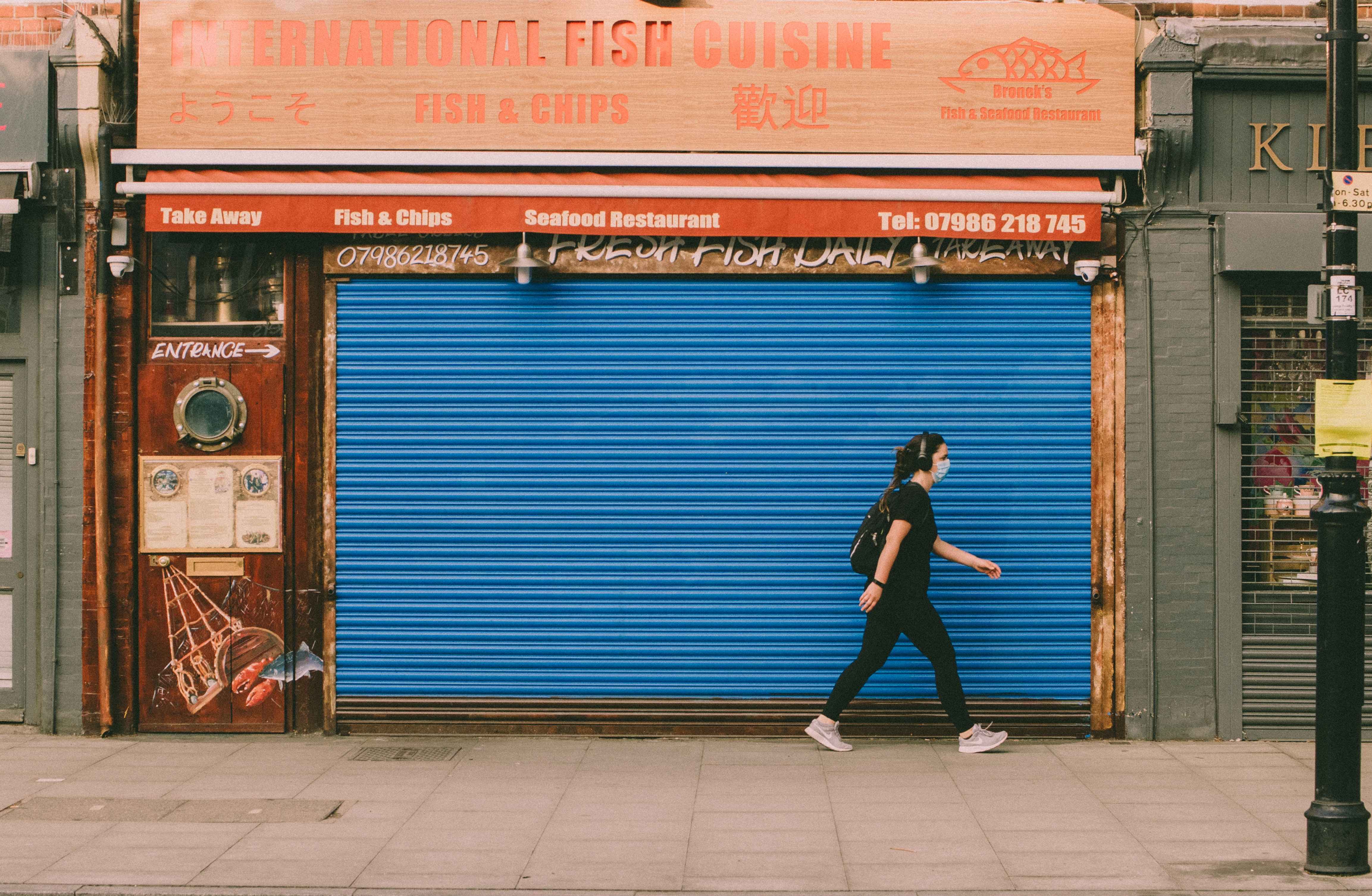 A person with a mask walking by a closed small business